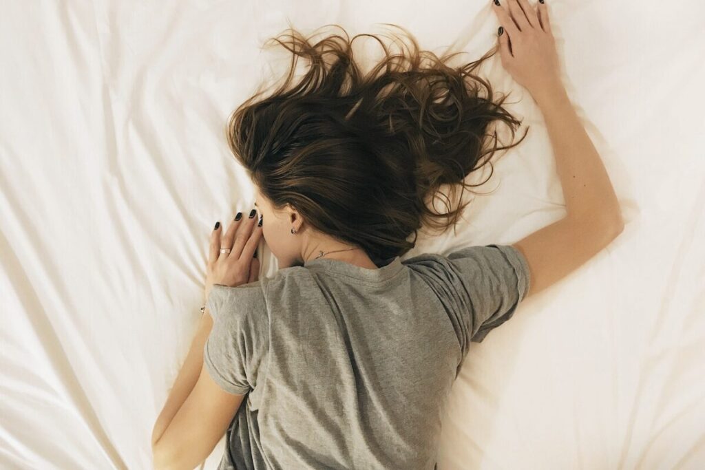 白いシーツを敷いたベッドの上に女性がうつ伏せに寝ている。