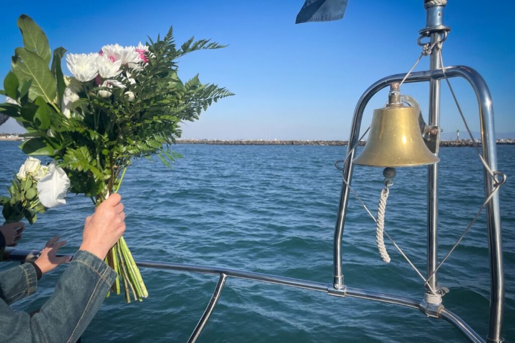 海の様子をクルーザーから撮影している写真。右側にベル、左側に白い供養花を持っている人の手元が写っています。
