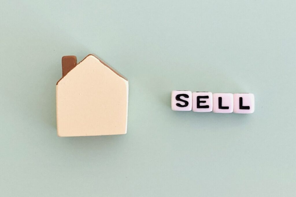 ミニチュアの家の横に、4つのサイコロのようなもの。それぞれに「SELL」と書いている。背景が淡いブルー。