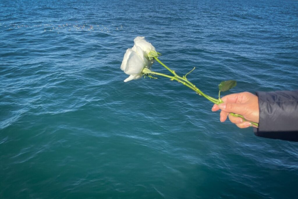海に向かって白い花を手向けようとしている人の手元