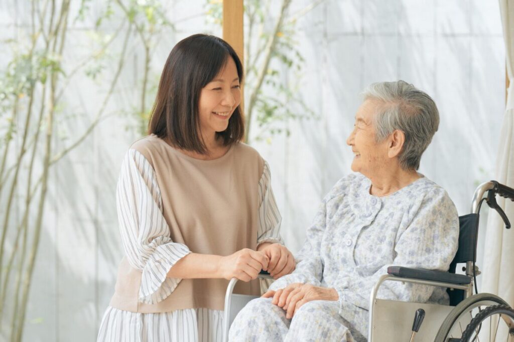 車椅子に座った高齢女性の横に中年の女性が笑い合っている。